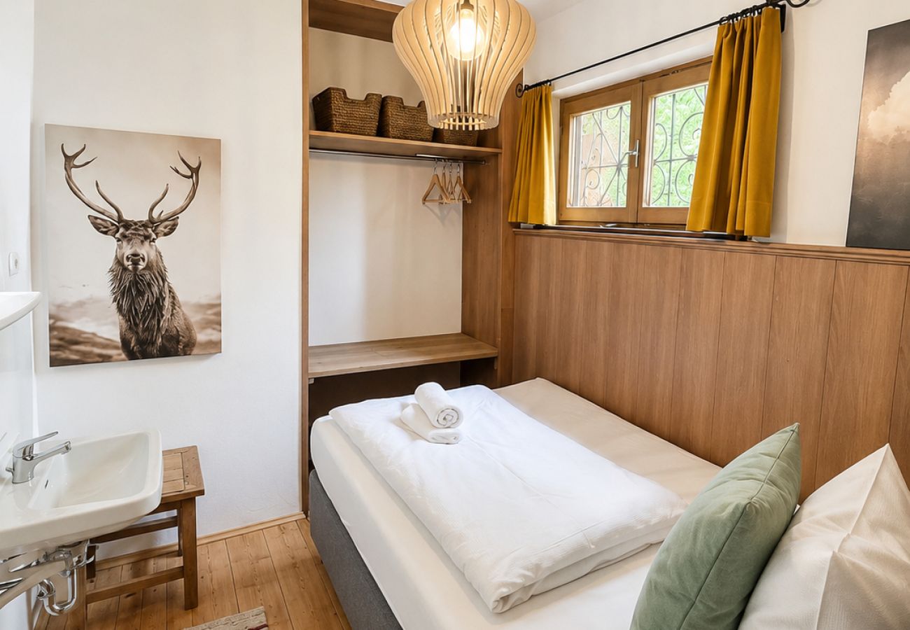 Kleines Schlafzimmer im Chalet Kirchberg in Tirol mit Bett, Holzwand, Fenster und Hirschbild
