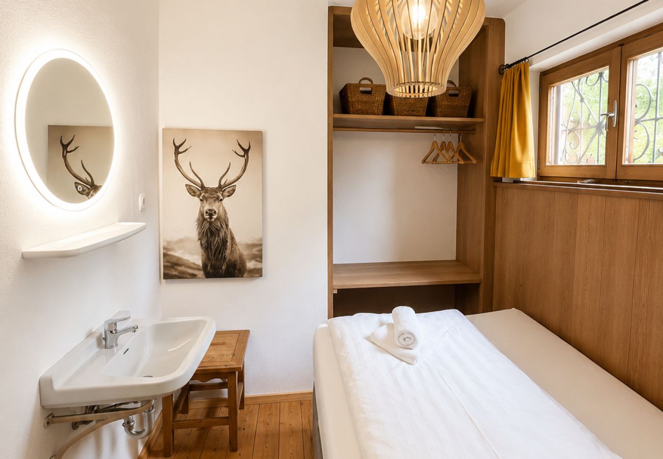 Einzelzimmer im Chalet Kirchberg in Tirol mit Einzelbett, Waschbecken, Spiegel, Holzwänden und Teppich